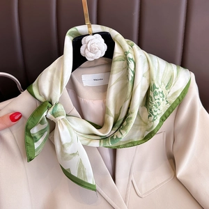 Elegant green floral silk-like square scarf styled on a beige blazer collar for women