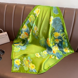 Green silk scarf with yellow lotus pattern displayed on a classic leather sofa