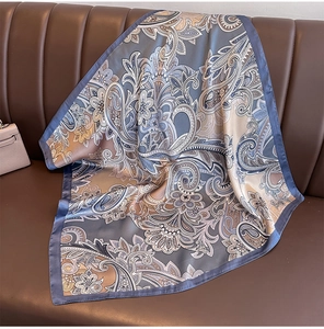 Detail of paisley silk-like square scarf draped on a leather sofa with elegant luster