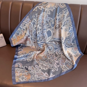 Elegant blue and gold paisley satin square scarf displayed on a leather surface
