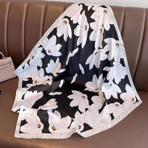 Élégant foulard en soie noir avec imprimé magnolia posé sur un canapé en cuir