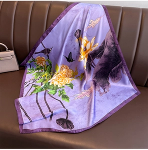 Detail of a purple silk square scarf with floral patterns draped on a brown leather sofa