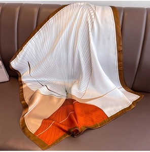 Macro view of silky scarf with orange and brown geometric patterns on leather sofa