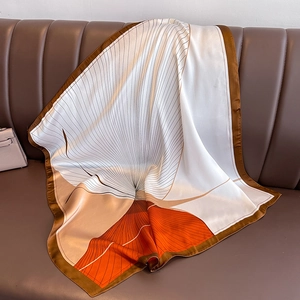 Minimalist silk scarf with orange and brown geometric patterns draped on a sofa