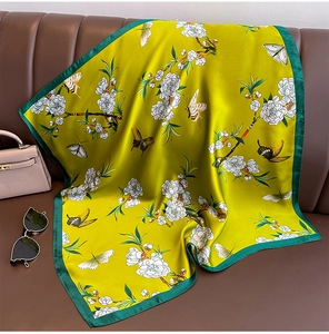 Dettaglio del foulard in seta gialla con fiori bianchi e farfalle su sfondo di pelle