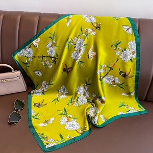 Elegante sciarpa in seta gialla con stampa di fiori e farfalle su un divano in pelle