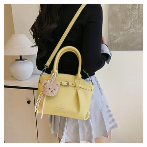 Detail view of yellow leather handbag featuring litchi texture and cute bear pendant