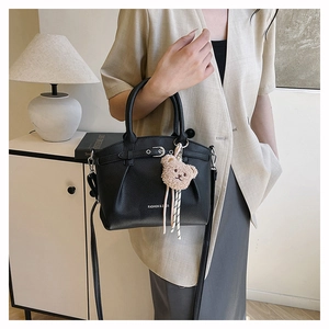 Close-up of black lychee grain leather bucket bag with cute plush bear charm detail