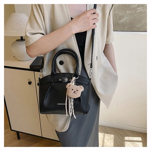 Detailed view of black leather bucket bag with litchi texture and cute bear charm