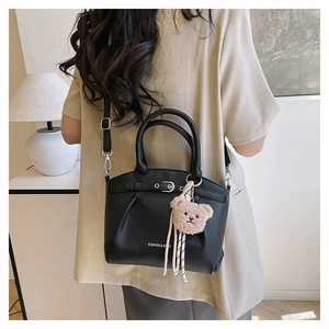 Close-up of black lychee leather bag with teddy bear charm and adjustable strap detail