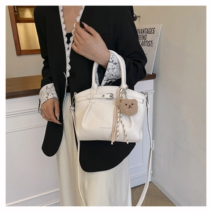 Detail of white lychee leather handbag with plush bear charm on black blazer model