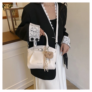 Detail of white lychee leather bucket bag featuring a cute brown plush bear charm