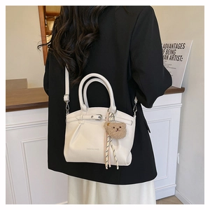 Detailed view of a white lychee leather tote bag featuring a cute teddy bear charm