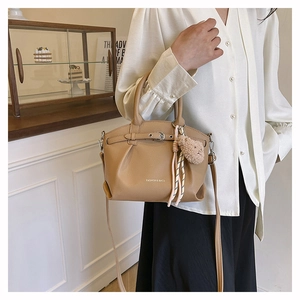 Detail of khaki textured leather handbag with logo and plush bear charm on a table