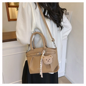 Detail of tan pebble leather tote bag with teddy bear charm and striped scarf on model