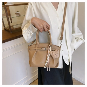 Detail of khaki pebbled leather bucket bag with plush bear charm and woven tassel detail
