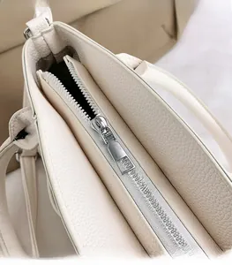 Close-up of silver metal zipper detail on beige lychee texture leather handbag