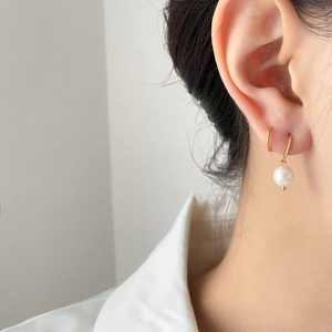 Detailed close-up of a minimalist gold hoop earring with a dangling white round pearl