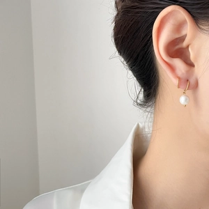 Detail of elegant gold hoop earrings with white round pearl drop worn by female model
