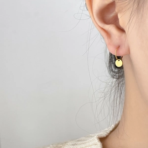 Close-up of a gold disc drop earring with a polished finish worn on a model's ear