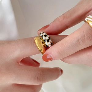 Primer plano de anillo dorado grueso y anillo de esmalte con patrón de damero blanco y negro