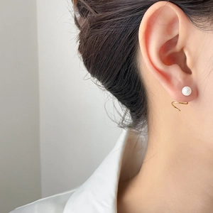 Detailed view of elegant gold spiral earring with pearl on model's ear in soft light
