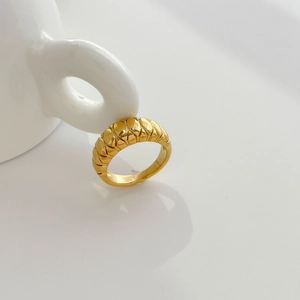 Detalle macro de anillo de cúpula dorado con diseño trenzado sobre fondo blanco minimal