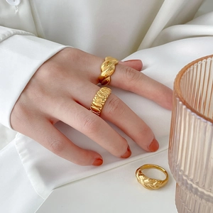 Detalle de anillos dorados trenzados y acanalados junto a un vaso de cristal