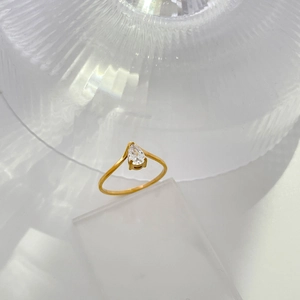 Detail of 18K gold plated titanium ring with pear-cut zircon on textured glass background