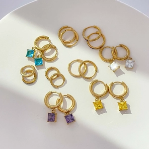 Detailed macro view of colorful square zircon charms and gold huggie hoop earrings