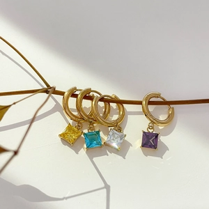Detail of square colorful zircon drop earrings with gold hoops on artistic branches