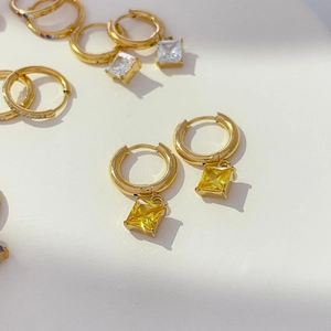 Macro shot of gold hoop earrings with square yellow and white zircon pendants