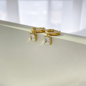 Detailed close-up of gold hoop earrings with square cubic zirconia on stone background