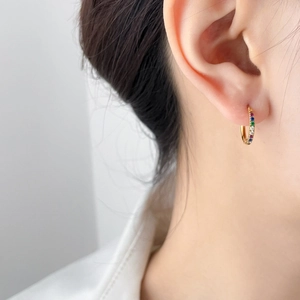Close-up of model wearing small gold hoop earrings with multi-colored rainbow cubic zirconia