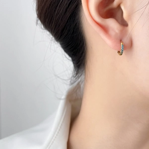 Detailed close-up of small golden hoop earrings featuring micro light blue zircon stones