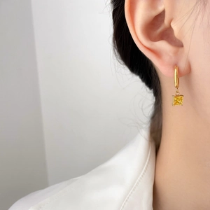 Close-up of a woman wearing a gold hoop earring with a square yellow zircon pendant