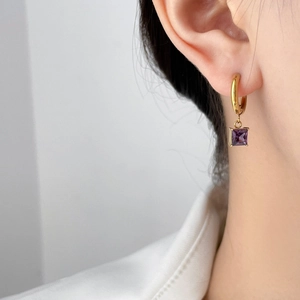 Close-up of small gold hoop earring with square purple zircon pendant worn on ear