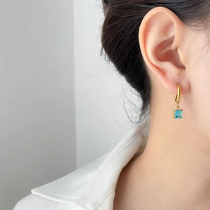 Elegant gold hoop earrings with a square blue zircon pendant shown on a model
