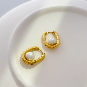 Detail of U-shaped gold earrings with embedded white pearl on a ceramic plate