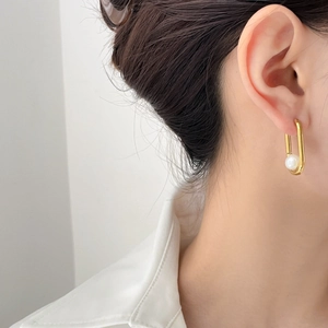Close-up of golden U-shaped pearl earrings worn by a model in a minimalist style