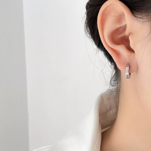Close-up of polished silver geometric C-shape hoop earrings worn by a female model