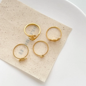 Close-up of 4 gold rings with butterfly, heart, and hugging hand designs on linen fabric