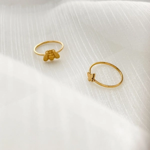 Macro detail of 18K gold plated minimalist bee and butterfly rings on white fabric