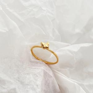 Detail shot of a delicate 18K gold plated butterfly ring on a textured white background