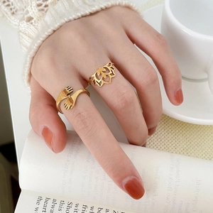 Detailed close-up of gold hollow lotus ring and embrace hand design on a female model