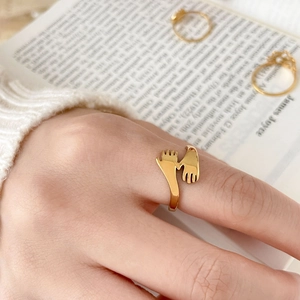 Macro detail of gold-plated hugging hands ring showing the polished texture and open band