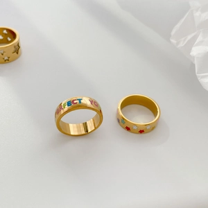 Détail de bagues dorées avec lettres colorées et motifs d'étoiles sur fond blanc