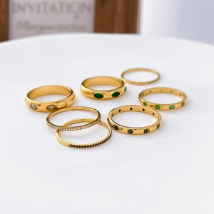 Detail of gold-plated rings with green and white zircons on a white minimalist display