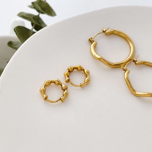 Detailed view of organic gold wavy hoop earrings on a minimalist ceramic plate