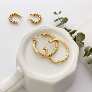 Detail of two pairs of gold hoop earrings with smooth and twisted textures on ceramic surface